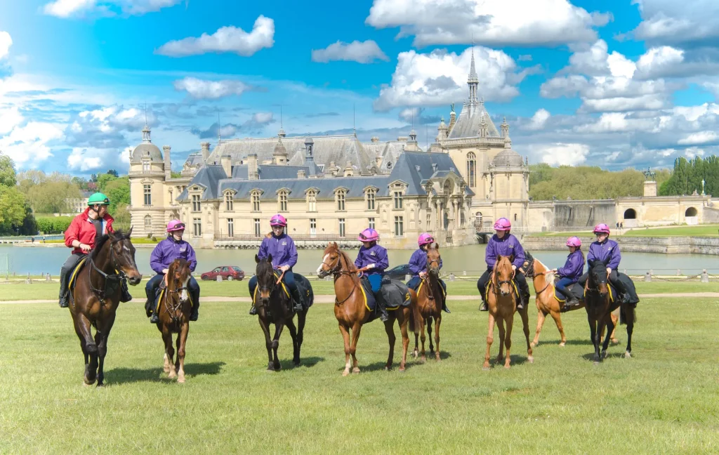 Groupe de cavaliers en tenue violette s'entraînant sur la pelouse devant le château de Chantilly par temps clair.